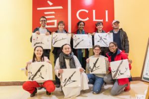 A group holds up ink paintings of bamboo in front of the CLI sign