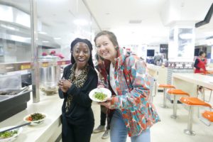 Two women laugh while holding a plate of greens in a cafeteria