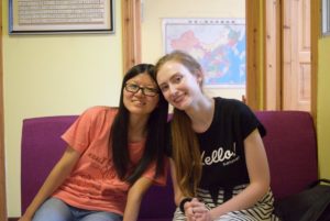 Two women sit close together on a sofa and smile