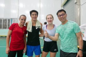 Four people in sports clothes give thumbs up at an indoor court