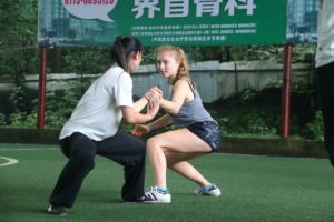 Two women practice a martial arts stance on a turf field