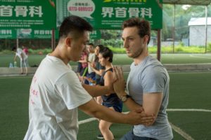 An instructor corrects a student's martial arts stance on a field