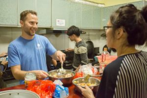 A smiling man stirs a pot of filling during a cooking in a kitchen