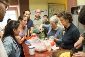 A group prepares food together at a crowded kitchen table beside a wall map