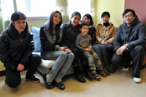 Six people and a child sit together on a sofa by a window
