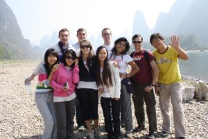 A group poses on the pebbled Li River shore as one man waves