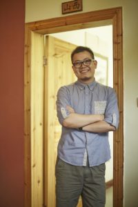 A man with crossed arms stands smiling in a doorway