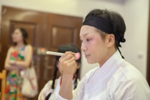 A performer applies stage makeup before a traditional show