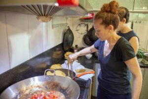 A woman cooks tomatoes in a large wok as another woman watches