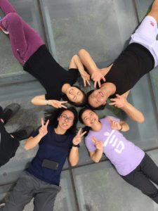 Five friends lie in a circle with their heads together, seen from above