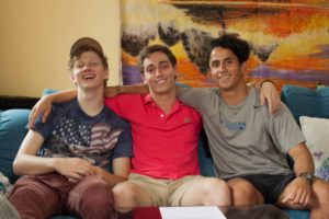 Three friends sit on a sofa with their arms around each other