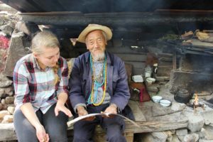 A woman sits beside a bearded man in a straw hat by an open hearth