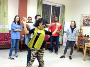 A woman dances in a green scarf while a group watches in a lounge