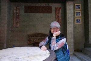 A woman sits smiling at a round stone table in a courtyard