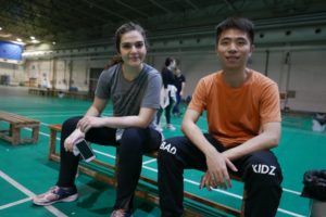 A woman and a man sit on a bench in an indoor sports hall