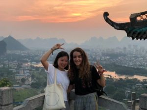 Two women make peace signs at a lookout over Guilin under an orange sky