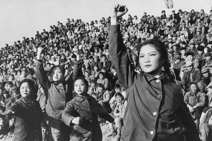 a black and white photograph showing a large group of people with three young Chinese women in the foreground, two with their fists raised