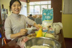 A smiling woman prepares ingredients beside a bag of flour and corn