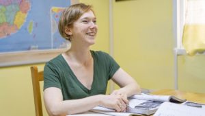 A smiling student sits at a table with an open textbook