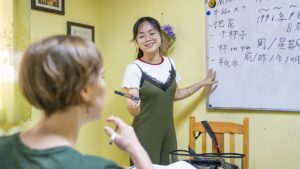 A teacher points to a whiteboard of characters while a student listens