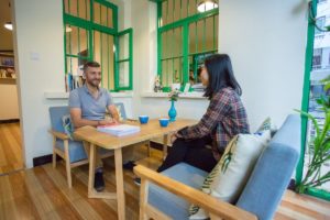 A student and teacher sit at a small table in a bright classroom