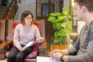 A teacher reads from a paper with a student in a wood-paneled room