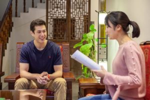 A student smiles as a teacher reads to him from a page