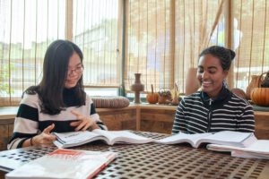 A student and teacher read open textbooks at a table by the window