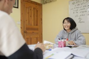 A teacher smiles across a table of books at her student
