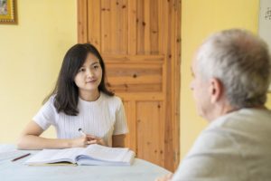 A teacher smiles at a student across a table with an open book