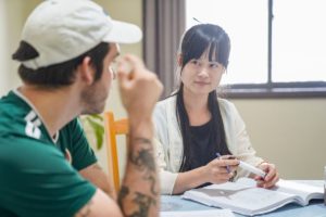A student in a cap rubs his eye while a teacher looks on
