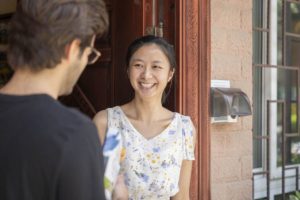 A smiling woman chats with a man in glasses at a doorway