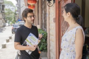 A student holding a textbook talks with a teacher outside the building