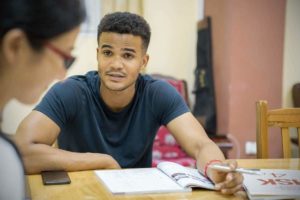 A student looks up from his textbook across the table from his teacher