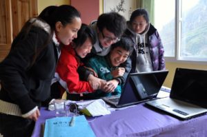 A group crowds around laptops at a table and laughs