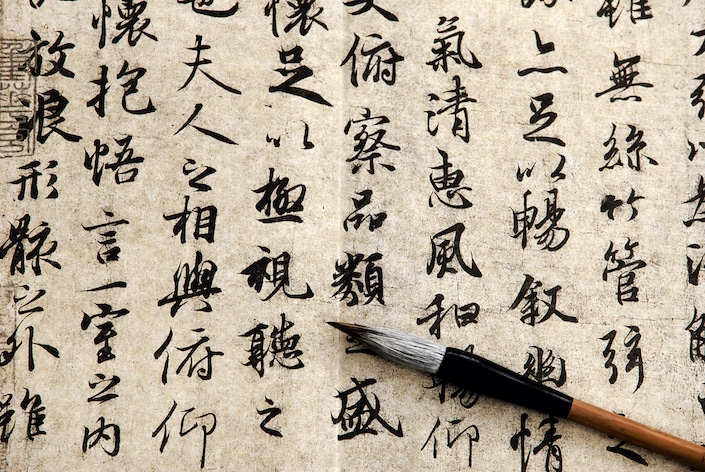 Chinese characters written on a piece of paper with a traditional Chinese calligraphy brush laying across it