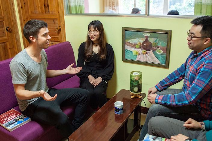 a western man, Chinese woman and Chinese man sitting together on sofas talking with a long, low wooden table between them