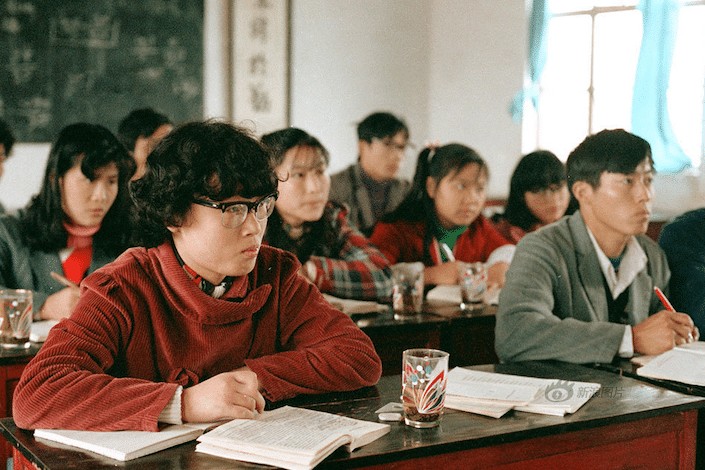 a photo from the 1980's of Chinese university students sitting at desks in a classroom 