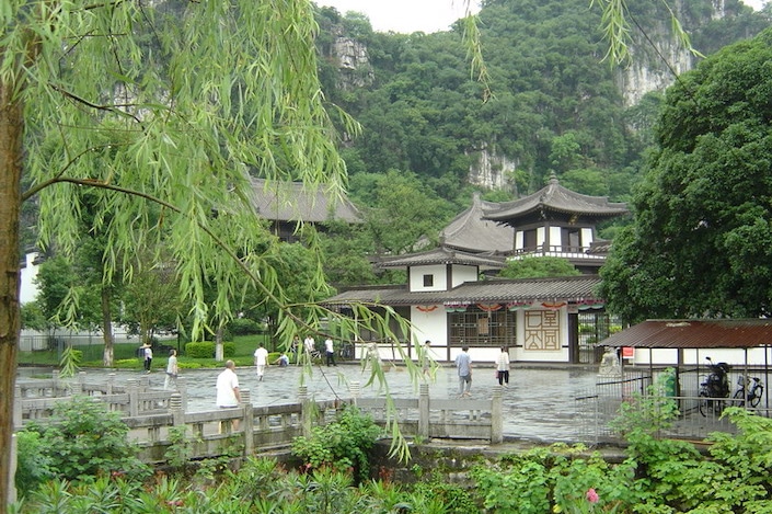 a white traditional Chinese building surrounded by a walkway and flanked by mountains in Guilin's Seven Star Park