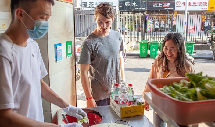 Young American boy and Chinese girl ordering food from a Chinese man at a food stall