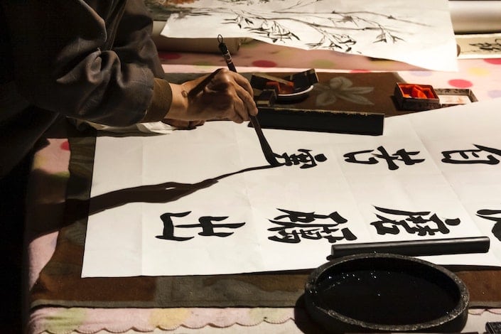 una mano que sostiene un pincel de caligrafía escribiendo caracteres chinos en una hoja larga de papel