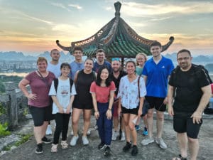 A group stands under a hilltop pavilion at sunset