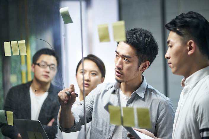 jeune entrepreneur asiatique d'une petite entreprise dessinant un diagramme sur du verre lors d'un atelier d'équipe au bureau discutant et formulant des stratégies commerciales