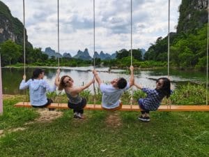 Four people swing on rope swings by a lake below karst peaks