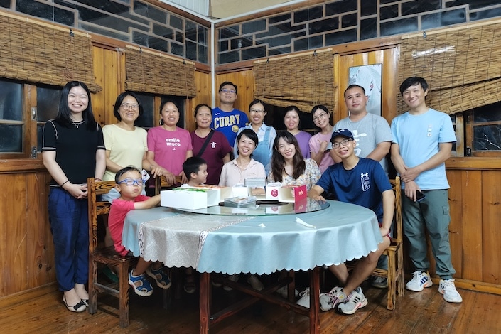 一群中国人站在摆姿势拍照，面前摆着一张圆形餐桌
