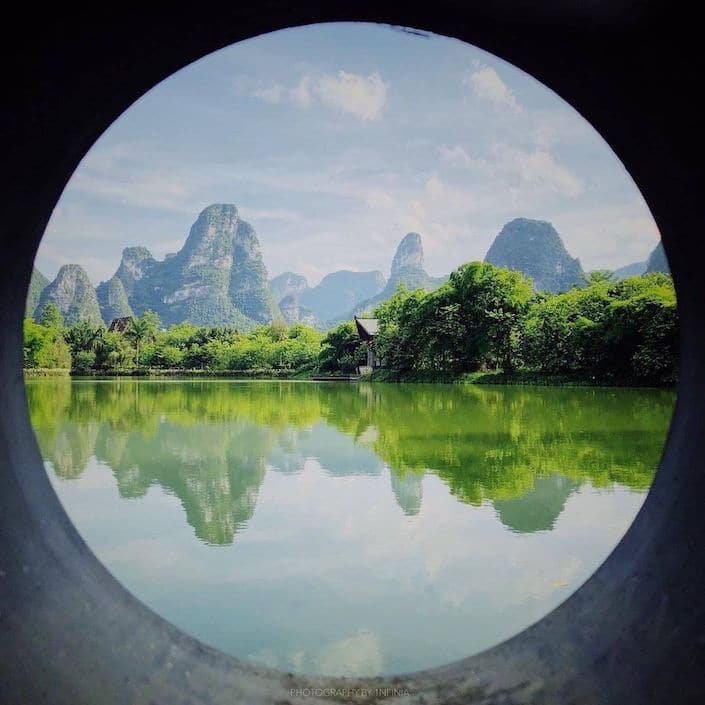 view of karst guilin mountains with water in foreground through circular pipe