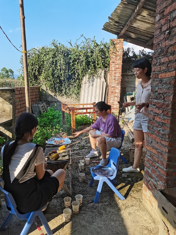 三个中国人在户外砖墙旁准备食物