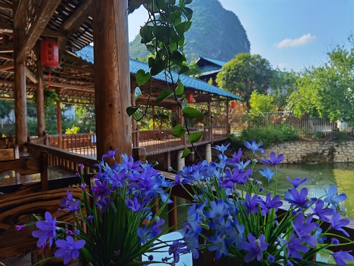purple flowers in a wooden veranda bridge over water with a karst mountain and blue sky in the background