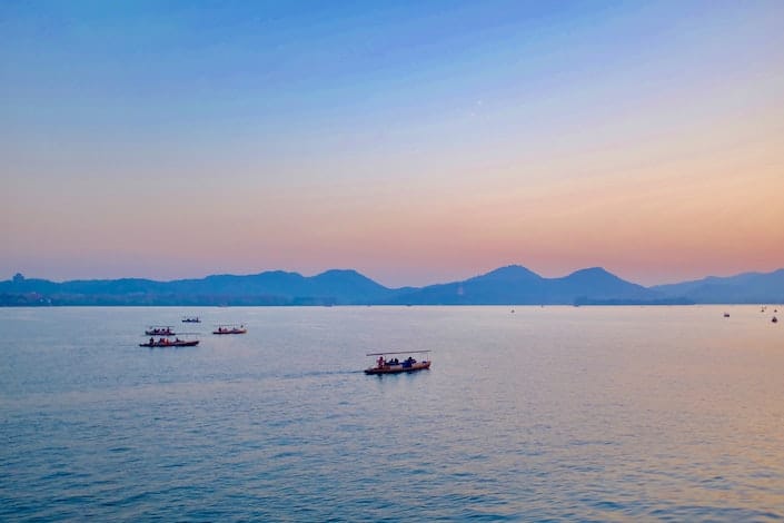 黄昏时分，中国杭州西湖上的几艘小船，背景是山丘