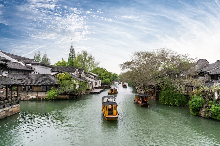Barcos tradicionales chinos flotando río abajo entre casas tradicionales chinas en una ciudad acuática en las afueras de Hangzhou